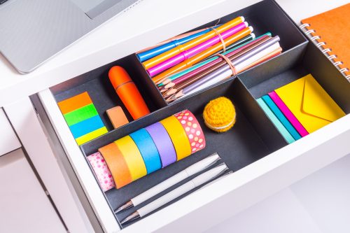 Opened office desk drawer with brightly colored stationery items.